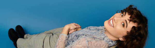 Charming young woman lies on her side, showing off a beautiful smile while dressed fashionably.