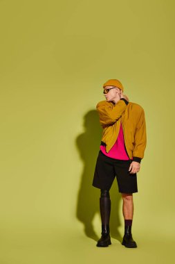 Protez bacaklı yakışıklı genç adam canlı bir arkaplan karşısında şık kıyafetler giyiyor..