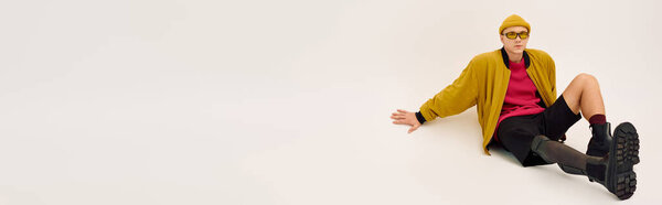 Young man with a prosthetic leg poses stylishly in fashionable attire against a plain backdrop, banner