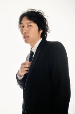 Tarz sahibi genç Asyalı bir adam kendine güvenerek siyah bir takım elbise giyer..