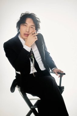 Kendine güvenen genç Asyalı adam modern modayı sergileyerek bir yönetmen koltuğuna şık bir şekilde oturur..