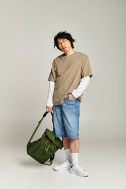 Genç Asyalı adam, modern gençlik kültürü ve tarzını somutlaştıran modaya uygun bir çantayla kendinden emin bir şekilde poz veriyor..