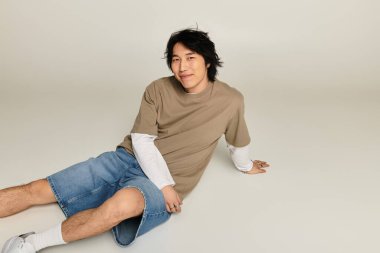 Yakışıklı Asyalı genç adam yerde rahatça oturuyor, modern şehir modasını sergiliyor..