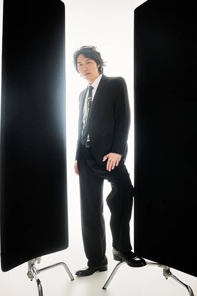 A stylish young Asian man stands between two black panels, exuding charm and confidence.
