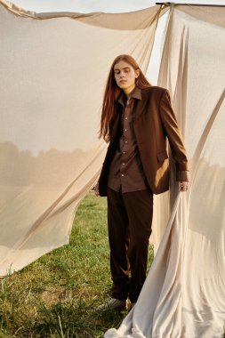 Zarif genç adam kendine güveni tam bir şekilde duruyor, doğanın yumuşak perdeleriyle çevrili..