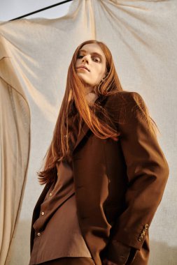 Uzun saçlı, genç ve yakışıklı bir adam şık ve modern kıyafetlerle ayakta duruyor..