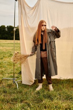 Uzun saçlı yakışıklı genç adam, sakin bir tarlada kendine güvenen modaya uygun bir şekilde poz veriyor..