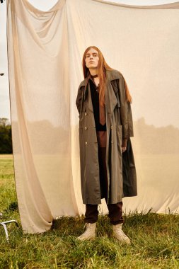 Uzun saçlı şık bir genç adam yumuşak bir arkaplanda güven içinde poz verir..