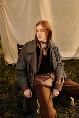 Uzun saçlı genç bir adam çimenlerde rahatlıyor, modaya uygun bir kıyafet ve kendine güven sergiliyor..