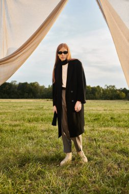 Moda kıyafetleri içinde genç bir adam, yumuşak bir gökyüzünün altındaki yemyeşil bir alanda güvenle duruyor..