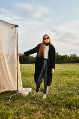 Uzun saçlı yakışıklı bir adam, sakin bir alanda arka planda dururken modayı kucaklıyor..