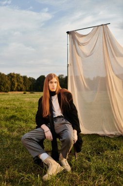 Uzun saçlı genç bir adam açık havada otururken kendine güvenini gösteriyor..