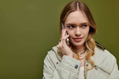 Açık renk ceketli güzel bir kadın telefonuyla konuşuyor, modern moda anlayışını sergiliyor..