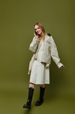 Genç bir kadın kendine güvenerek güler şık bir bahar kıyafetiyle, yeşil bir arka planda telefonla konuşur..