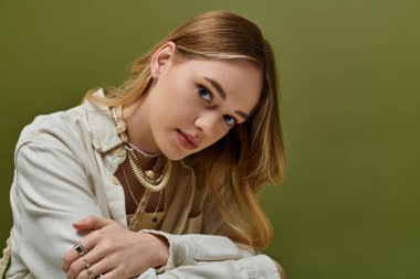 Dalgalı saçları olan genç bir kadın otururken şık bir bahar elbisesi içinde zarifçe poz verir..