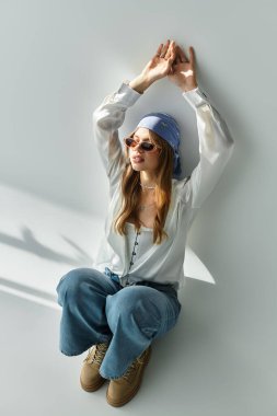 Genç bir kadın bahar kıyafetiyle gevşiyor, gri bir zemine neşeli bir hava yayıyor..