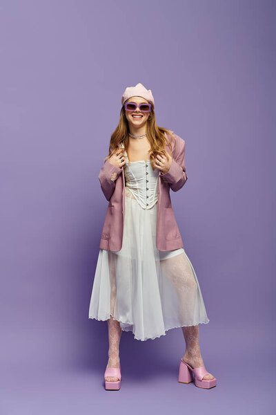 A young woman shines in a stylish outfit against a vibrant purple backdrop.