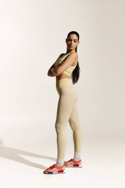 Kendine güvenen genç bir kadın, minimalist bir arkaplana karşı zarif bir spor bakışı sergiliyor..