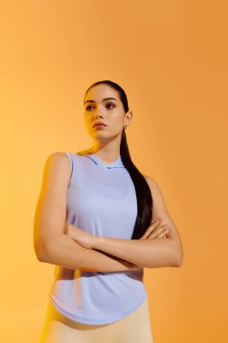 Kollarını kavuşturmuş kendine güvenen genç bir kadın sıcak turuncu bir zemine poz veriyor..