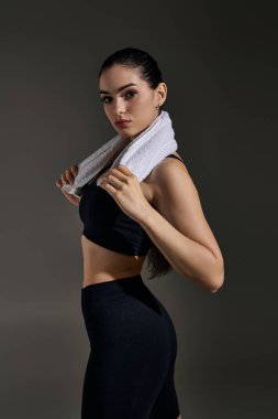 Boynunda havluyla kendine güvenen genç bir kadın atletizm pozisyonunda güçlü bir poz veriyor..