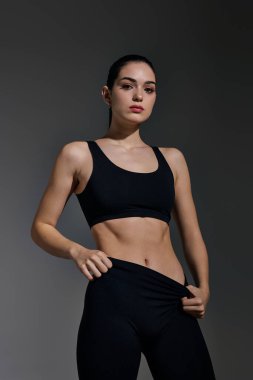 Kendine güvenen genç bir kadın atletizmini bir stüdyo çekimi sırasında gösterişli bir siyah kıyafetiyle sergiliyor..