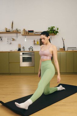Sportif bir kadın modern bir mutfak ortamında yoga yaparken mindere uzanır..