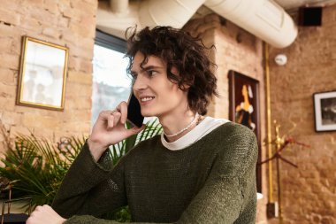 Genç ve yakışıklı bir adam şık bir kafede otururken telefonla konuşuyor.