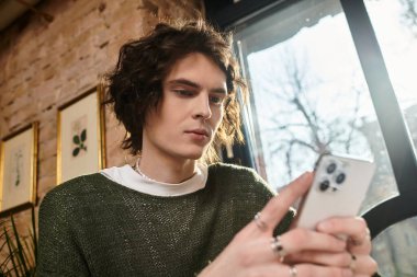 Bir kafede şık bir genç adam rahat bir atmosfer içinde mobil cihazıyla meşgul oluyor..