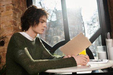 Genç adam, güneşli bir günde aydınlık bir kafede dinlenirken kitaba dikkatle odaklanır..