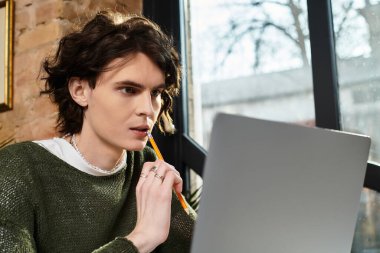 Genç ve yakışıklı bir adam canlı bir kafede dizüstü bilgisayarla çalışırken düşünceli bir şekilde düşünür..