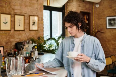 Genç, yakışıklı bir adam bir kafede oturup elinde kahve fincanı ile menüyü dikkatle inceliyor..