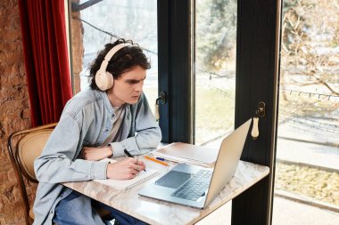 Genç bir adam bir kafede tek başına oturmuş, odaklanarak ve yaratıcılıkla çalışıyor..