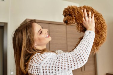Genç bir kadın, köpeğiyle otel odasında neşe dolu bir anın tadını çıkarıyor..