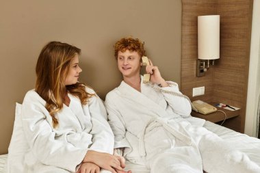 Otel bornozlu bir çift, eğlenceli bir telefon görüşmesi yaparken kaliteli zaman ve kahkaha geçirir.