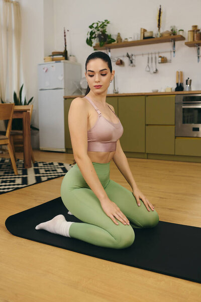 Relaxed young woman engages in yoga on a mat in a stylish home kitchen with modern decor