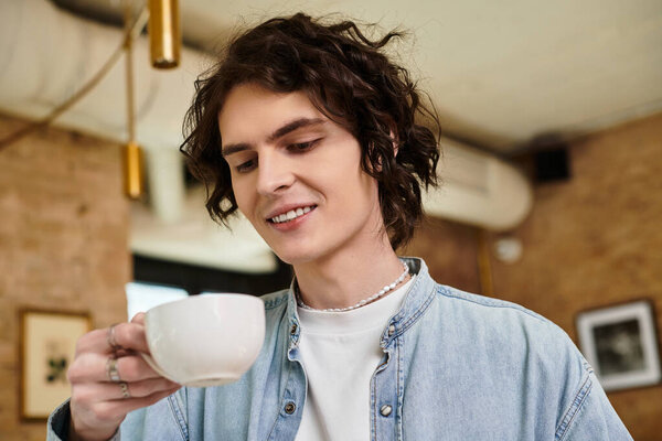 Молодой красивый парень наслаждается теплым напитком, расслабляясь в яркой атмосфере кафе.