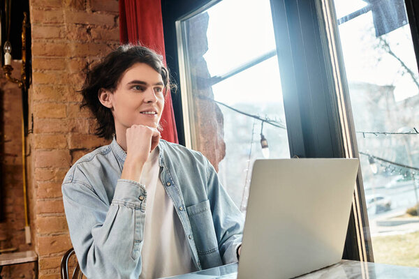 В уютном кафе молодой человек вступает в контакт со своим ноутбуком, наслаждаясь моментом.