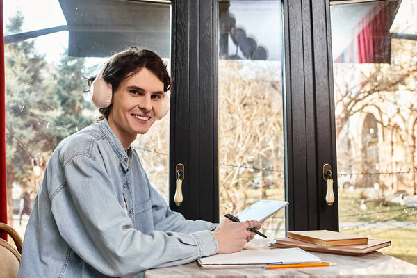 Веселый молодой человек в наушниках сидит за столом, учится и наслаждается спокойной атмосферой кафе.