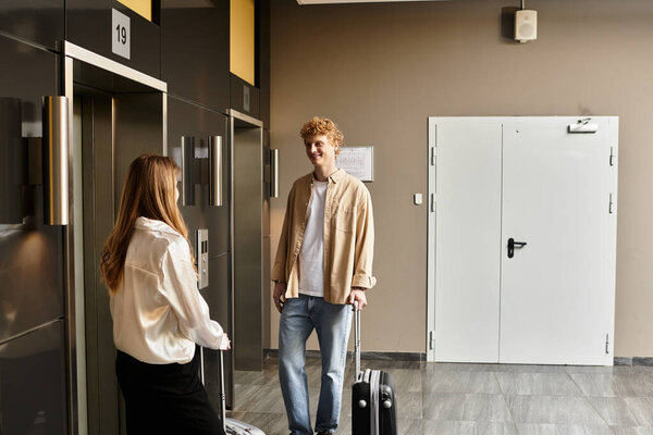 Delighted young couple stands together with luggage, enjoying each others company in hotel lobby.