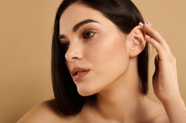 Genç kadın, sakin bir stüdyo ortamında poz verirken çarpıcı cildini ön plana çıkarıyor, güzelliği vurguluyor..