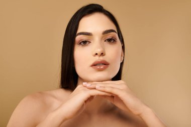 Genç bir kadın ışıldayan tenini sergiliyor. Çenesini ellerinin üzerinde dinlendirirken, ışıldayan bir güzellik..