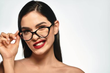 Kırmızı dudaklı, kendine güvenen genç bir kadın yumuşak, gri bir arka plana bakıyor..