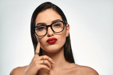 Kırmızı dudaklı ve gözlüklü kendine güvenen genç bir kadın cazibe ve zarafet yayar..