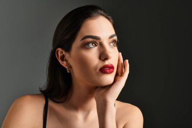 Kahverengi saçlı ve çarpıcı kırmızı dudaklı genç bir kadın düşünceli bir şekilde uzaklığa bakıyor..