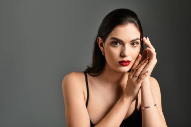 Kahverengi saçlı güzel bir kadın gri bir arka plana karşı zarifçe poz verir..