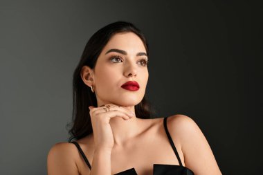 Kahverengi saçlı genç bir kadın güzelliğini koyu kırmızı dudaklarıyla sergiliyor, düşünceli bir poz veriyor..