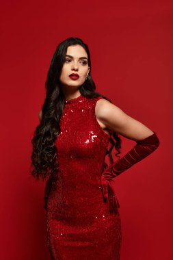 Kahverengi saçlı, çarpıcı genç bir kadın koyu kırmızı bir elbiseyle parlıyor, kendine güveni tam..