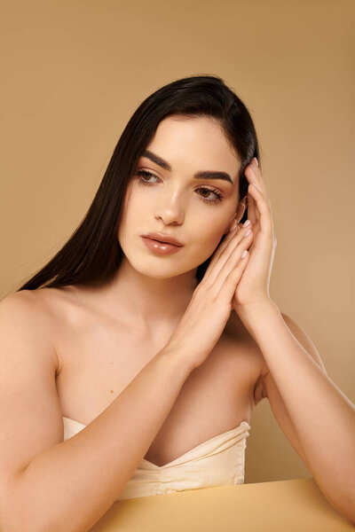 Молодая женщина расслабляется в студии с сияющей кожей, воплощая красоту и здоровье без особых усилий.