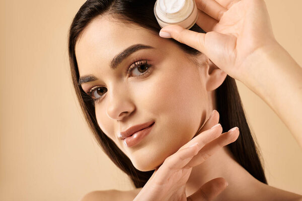 A young woman applies cream to her perfect skin, revealing a glowing and healthy complexion.