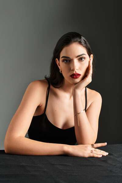 Молодая женщина с каштановыми волосами и красными губами элегантно позирует, демонстрируя свою красоту и изящество.